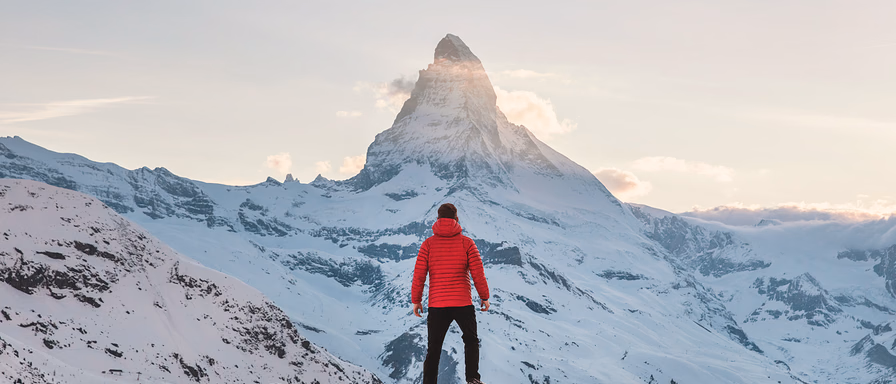 A man climbing a mountain and looking up at its peak in the distance.