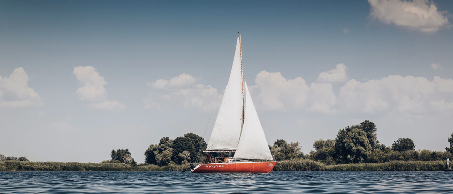 A sailboat with a red hull and white sail floating on a river.